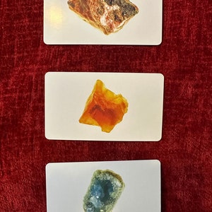 May include: Three cards displaying different mineral specimens. The top card shows a brown and white rock, the middle card features an orange mineral, and the bottom card displays a blue-green crystal. The cards are on a red background.