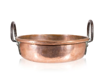 May include: A vintage copper pan with two iron handles. The pan has a rounded bottom and a slightly flared rim.