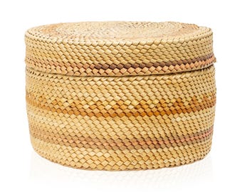May include: A round, woven basket with a lid. The basket is made of natural-colored straw with horizontal bands of light brown and pinkish-brown. The lid fits snugly on top, creating a storage container.