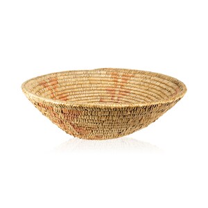 May include: A large, round, woven basket made of natural materials. The basket is light brown with hints of orange and has a smooth, slightly textured surface.