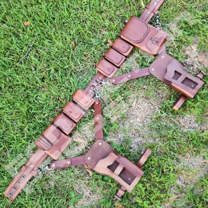 Puede incluir: Un cintur&oacute;n utilitario de cuero marr&oacute;n con m&uacute;ltiples bolsas y una funda, conectados por cadenas y correas de metal. El cintur&oacute;n est&aacute; dise&ntilde;ado con un patr&oacute;n de camuflaje y est&aacute; sobre hierba verde.