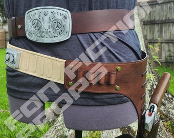 May include: A brown leather belt with a silver buckle featuring a detailed design. The belt has a beige fabric strap with a metal buckle and a brown leather holster with a metal buckle.  The text "BLASTER PISTOL DOES NOT COME WITH PURCHASE." is visible at the bottom of the image.