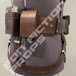 May include: A brown leather belt with a holster and a pouch. The belt has a silver buckle and is worn on a mannequin.
