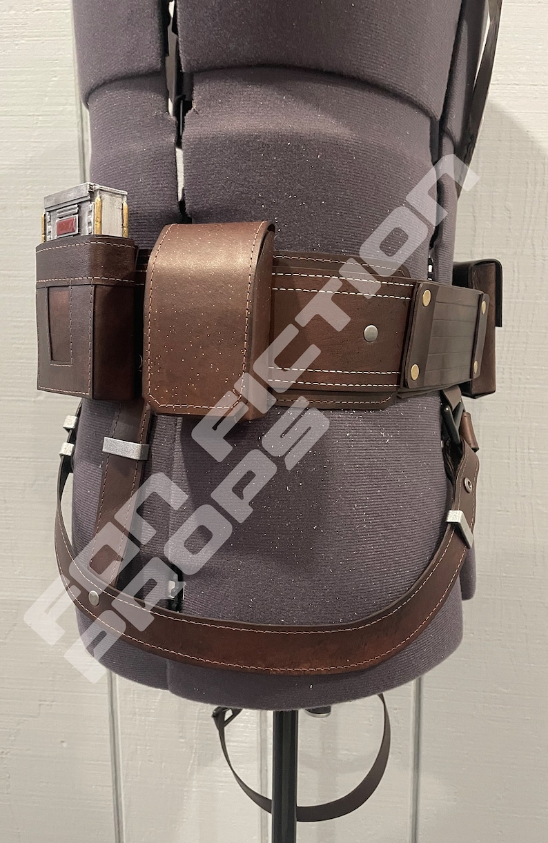May include: A brown leather belt with a holster and a pouch. The belt has a silver buckle and is worn on a mannequin.