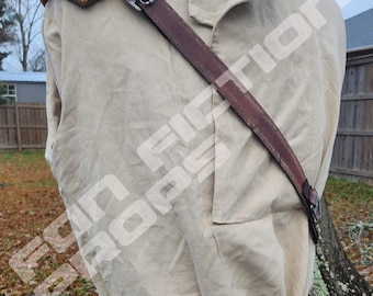 May include: A brown leather shoulder strap with a metal buckle attached to a yellow and white shoulder pad. The strap is worn over a beige shirt with a brown belt and a silver buckle. The text "REPLICA BELTS CAN BE PURCHASED ON A SEPARATE LISTING." is at the bottom of the image.