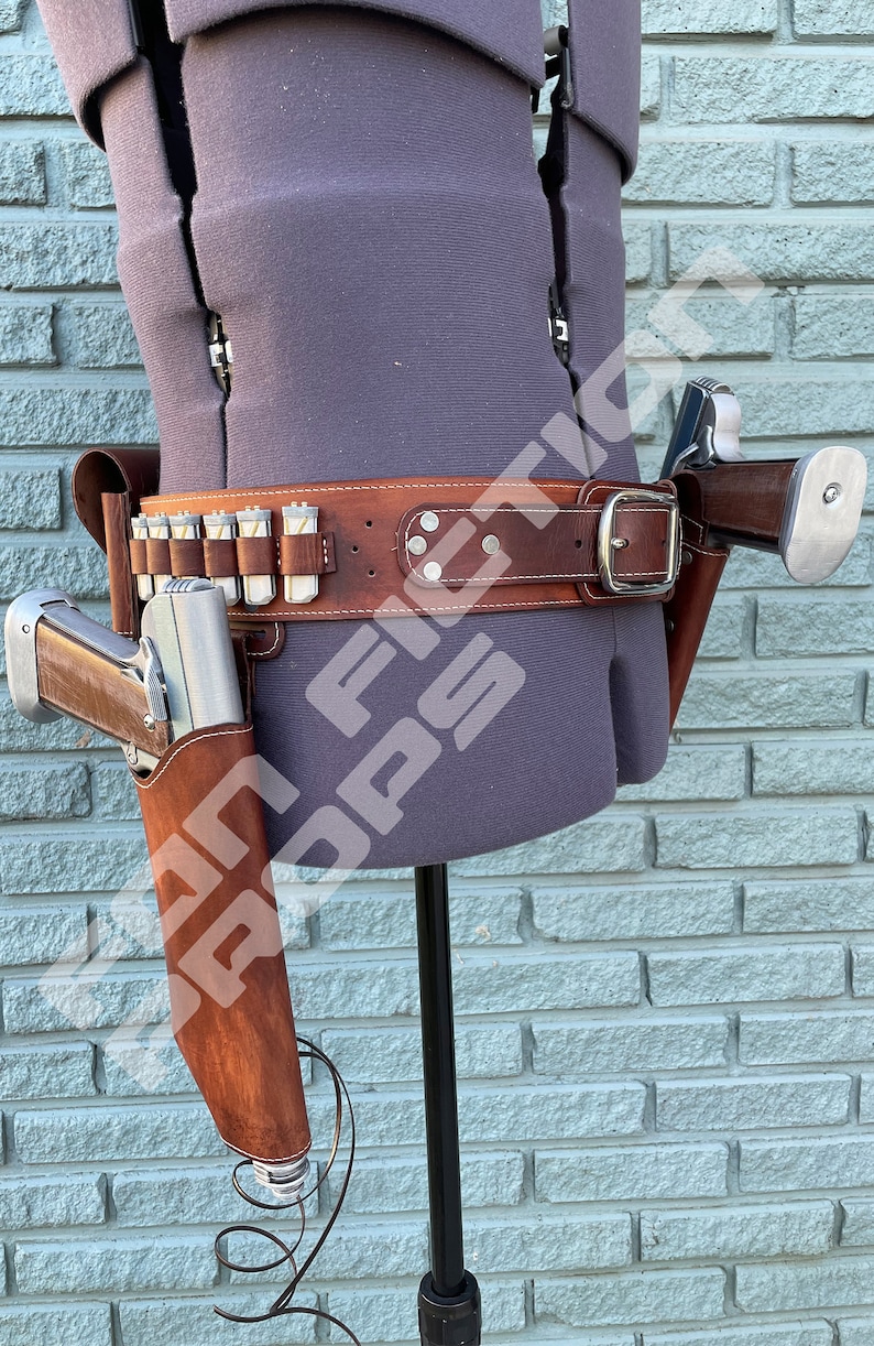 May include: A brown leather belt with a silver buckle and two holsters for pistols. The belt has a row of bullet loops and is worn on a mannequin.