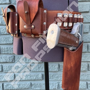 May include: A brown leather belt with multiple pouches and a holster for a silver pistol. The belt is worn on a mannequin with a grey shirt.