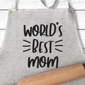 May include: A gray linen apron with black text that reads "WORLD'S BEST MOM". A wooden rolling pin is in the foreground.