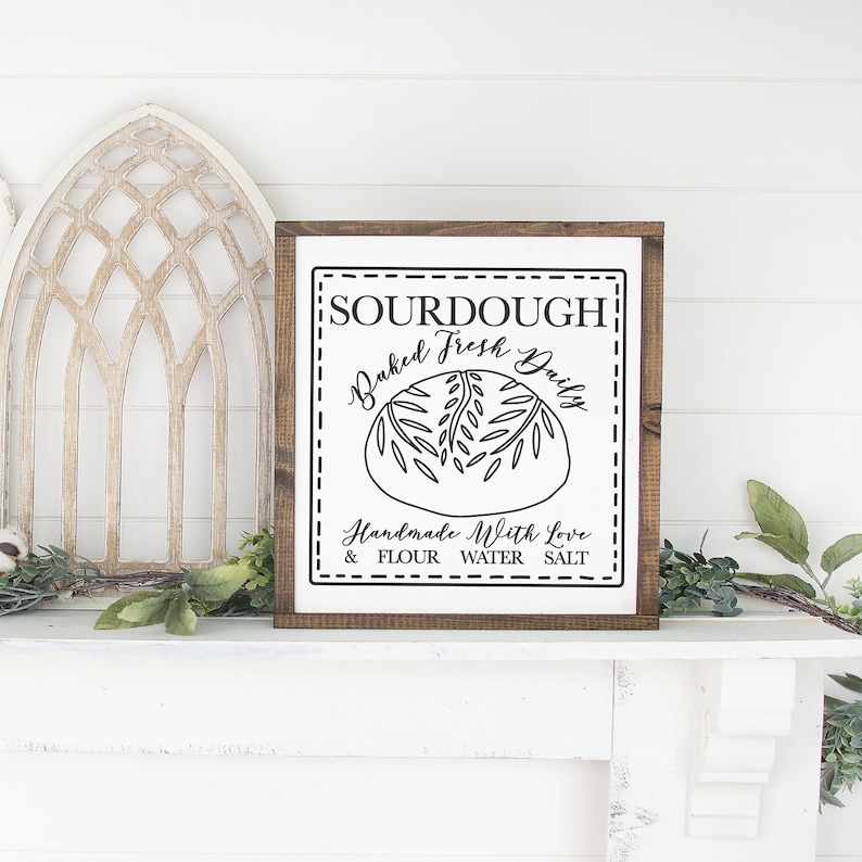 May include: White wooden sign with black text that reads "SOURDOUGH Baked Fresh Daily Handmade With Love & FLOUR WATER SALT". The sign features a black and white illustration of a loaf of bread.