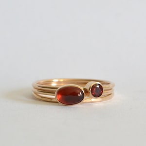 May include: A set of three gold rings with red gemstones. The rings are stacked on top of each other, with the largest ring on the bottom and the smallest ring on top. The gemstones are oval and round in shape.