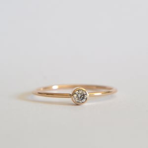 May include: A delicate gold band ring with a single, small, round diamond.