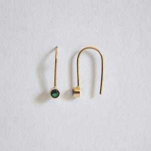 May include: A pair of gold hoop earrings with a small green gemstone on each earring.