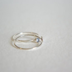 May include: Two silver rings, one with a small blue gemstone, are stacked on top of each other.