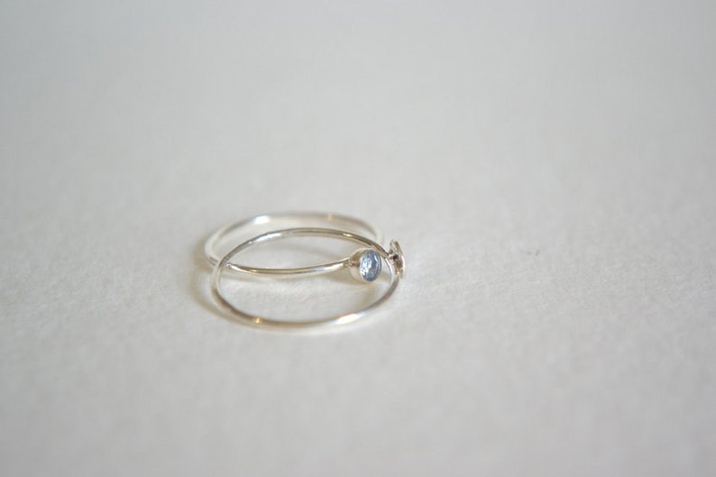 May include: Two silver rings, one with a small blue gemstone, are stacked on top of each other.
