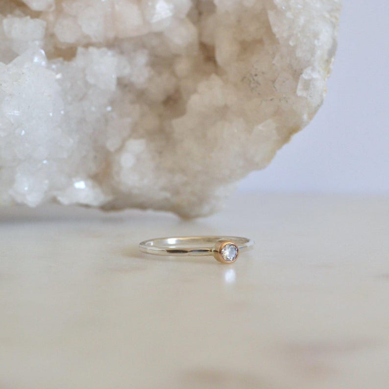 May include: A silver ring with a hammered texture and a small, clear gemstone set in a gold bezel.