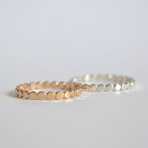 May include: Two delicate rings made of small, round beads. One ring is silver and the other is rose gold.