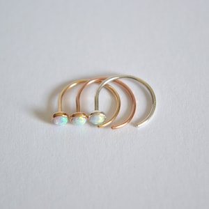 Pode incluir: Tr&ecirc;s argolas de nariz com pedras de opala. As argolas s&atilde;o de prata, ouro rosa e ouro.