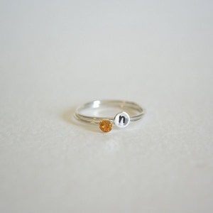 May include: A silver ring with a small orange gemstone and the letter "n" engraved on the band.