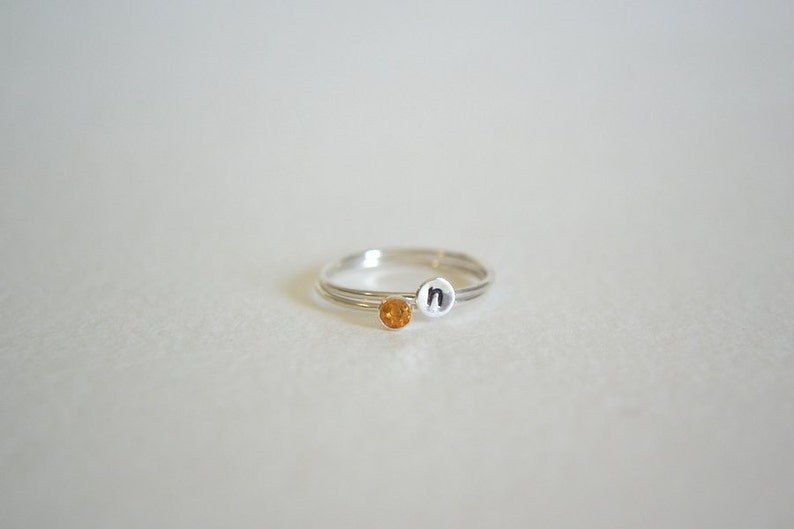 May include: A silver ring with a small orange gemstone and the letter "n" engraved on the band.