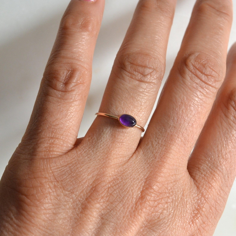 May include: A delicate gold ring with a small oval amethyst gemstone.