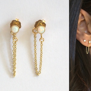 Peut inclure: Une paire de boucles d'oreilles en chaîne dorée avec des pierres d'opale. Les boucles d'oreilles sont conçues pour être portées avec la chaîne qui pend du lobe de l'oreille.