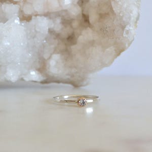 May include: A delicate silver ring with a small, clear gemstone set in a gold band.