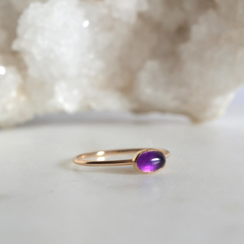 May include: A simple gold band ring with a purple amethyst gemstone.