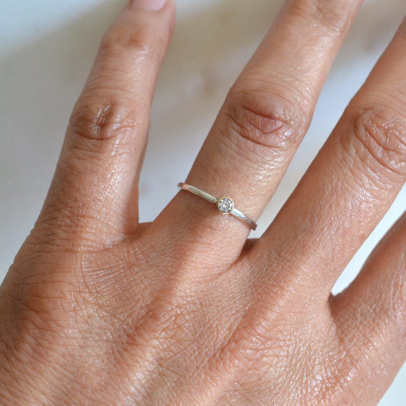May include: A simple silver band ring with a small, clear gemstone in the centre.