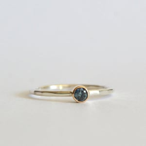 May include: A silver ring with a blue gemstone set in a gold bezel.
