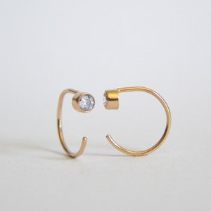 May include: A pair of gold hoop earrings with a small clear stone on each hoop.
