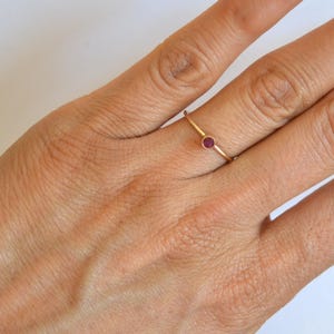 K&ouml;nnte beinhalten: Ein schlichter Goldring mit einem kleinen, runden, roten Edelstein.