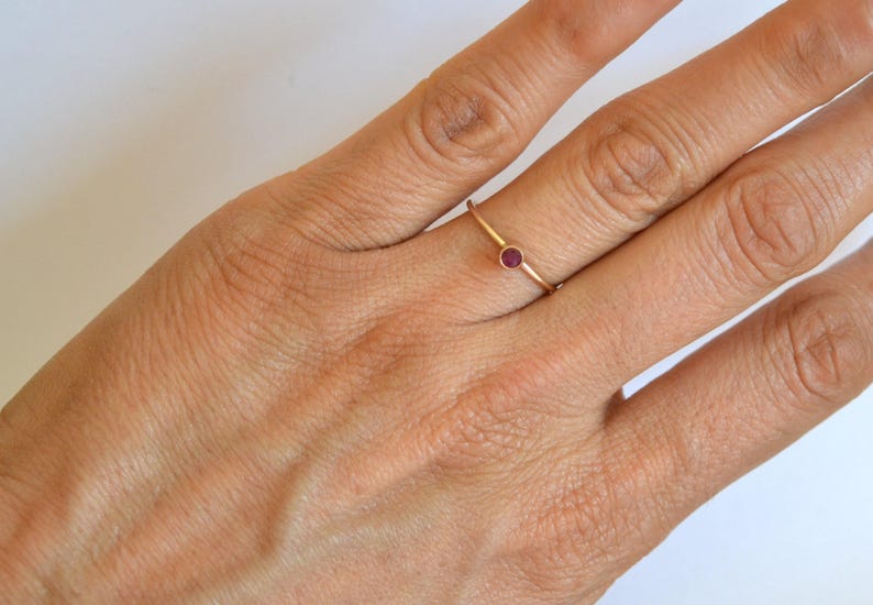 K&ouml;nnte beinhalten: Ein schlichter Goldring mit einem kleinen, runden, roten Edelstein.