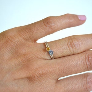 May include: A silver ring with a small yellow gemstone and a silver letter on the band.