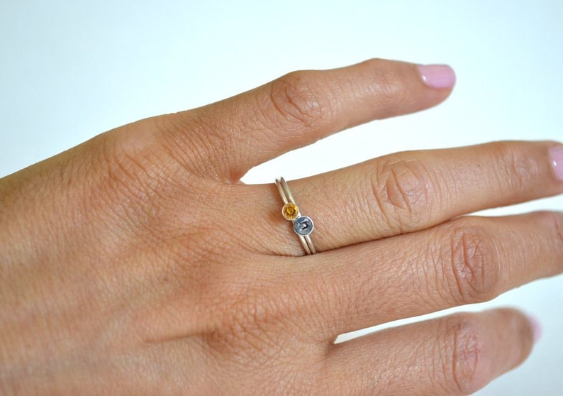 May include: A silver ring with a small yellow gemstone and a silver letter on the band.