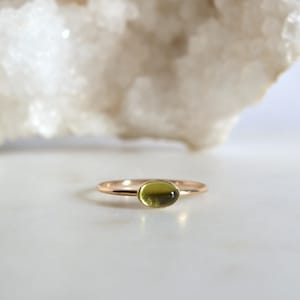 Puede incluir: Un delicado anillo de oro con una piedra ovalada verde claro.