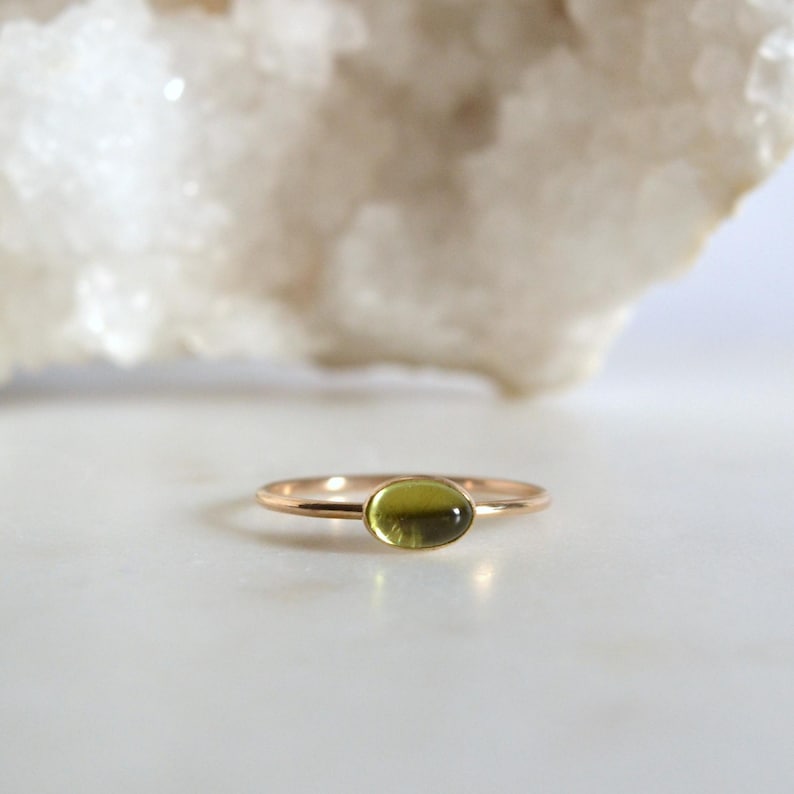 Puede incluir: Un delicado anillo de oro con una piedra ovalada verde claro.