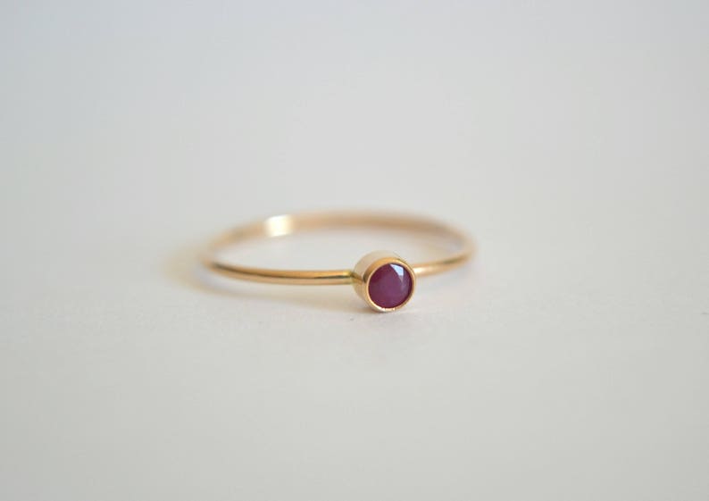 K&ouml;nnte beinhalten: Ein schlichter Goldring mit einem kleinen, runden, dunkelroten Edelstein.