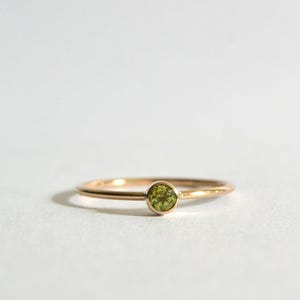 May include: A simple gold band ring with a small, round green gemstone set in the center.