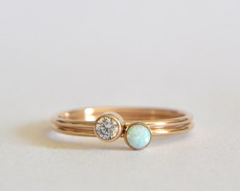 May include: Two gold rings with a single round diamond and a round opal gemstone.