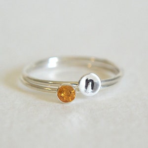 May include: A silver ring with a small orange gemstone and a silver charm with the letter 'n' on it.