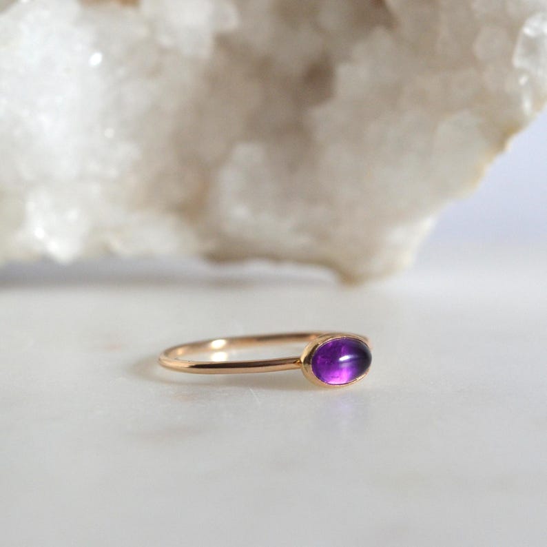May include: A delicate gold ring with a purple amethyst gemstone. The ring is simple and elegant, perfect for everyday wear.
