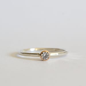 May include: A silver band ring with a single round diamond set in a rose gold bezel.