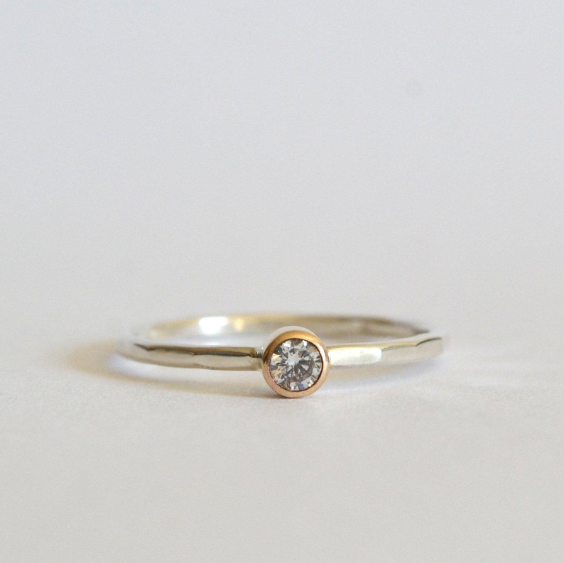 May include: A silver band ring with a single round diamond set in a rose gold bezel.
