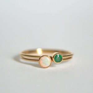 May include: A gold ring with two stones, one white opal and one green emerald.