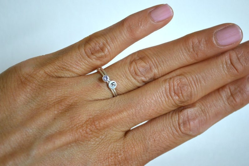 May include: A silver ring with a small purple gemstone and a letter 'K' charm.