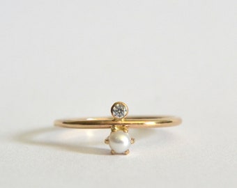 May include: A delicate gold ring with a small pearl and a tiny diamond accent.