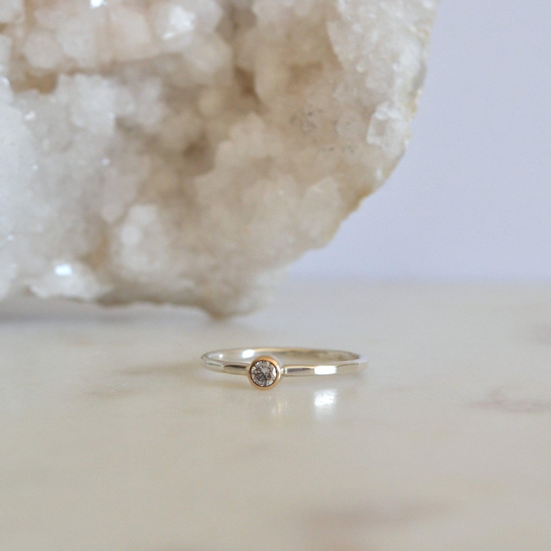 May include: A silver ring with a hammered texture and a small, clear gemstone set in a gold bezel.