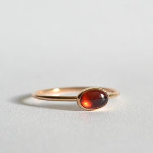 May include: A delicate gold ring with a single, oval-shaped, red gemstone set in the center.