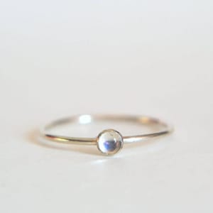 Puede incluir: Un anillo de plata con una piedra de luna redonda y blanca.