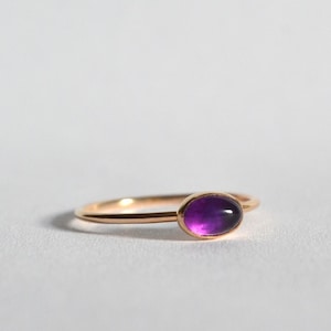 May include: A delicate gold ring with a purple oval amethyst gemstone.